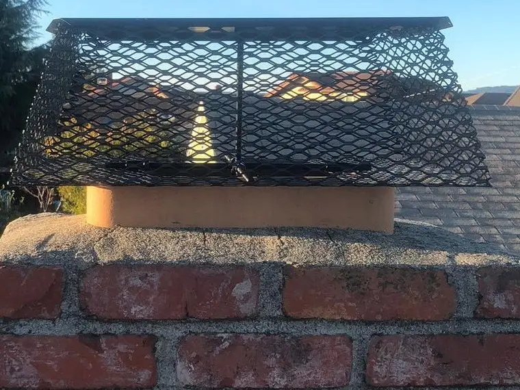 A red brick chimney topped by a wide black mesh lid over its flue